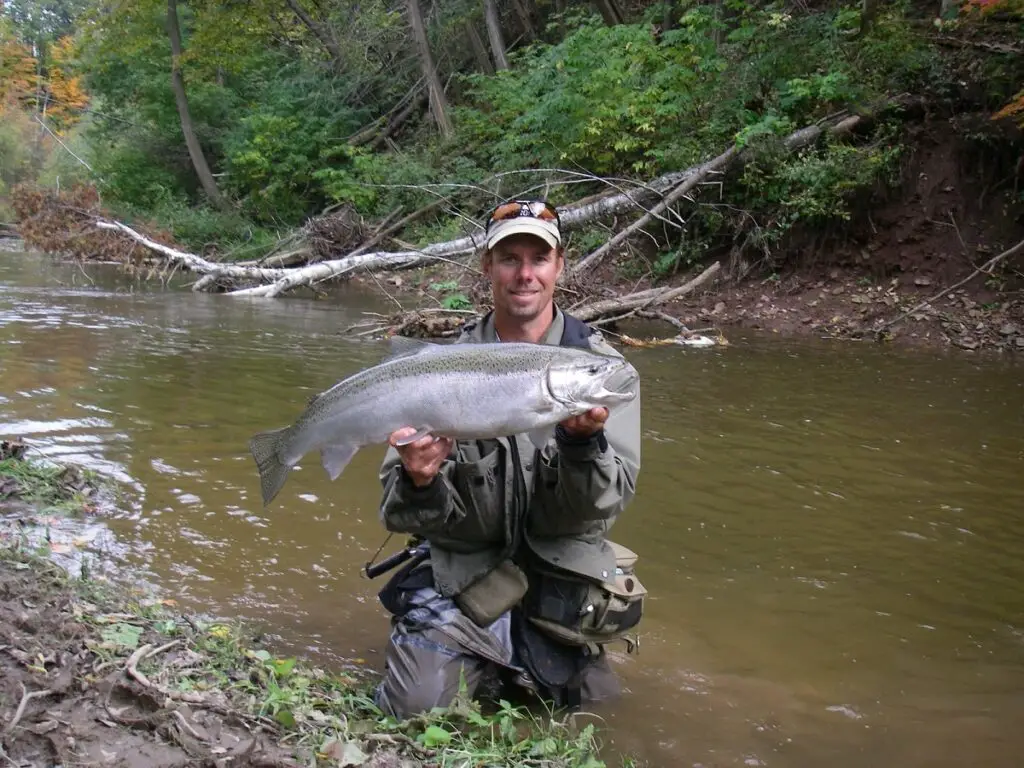 The author kneeling in a pair of waders while holding a big steelhead.